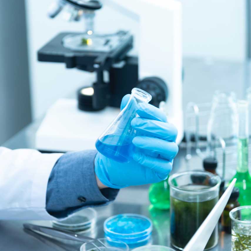 Gloved scientist examining a blue liquid among laboratory glassware